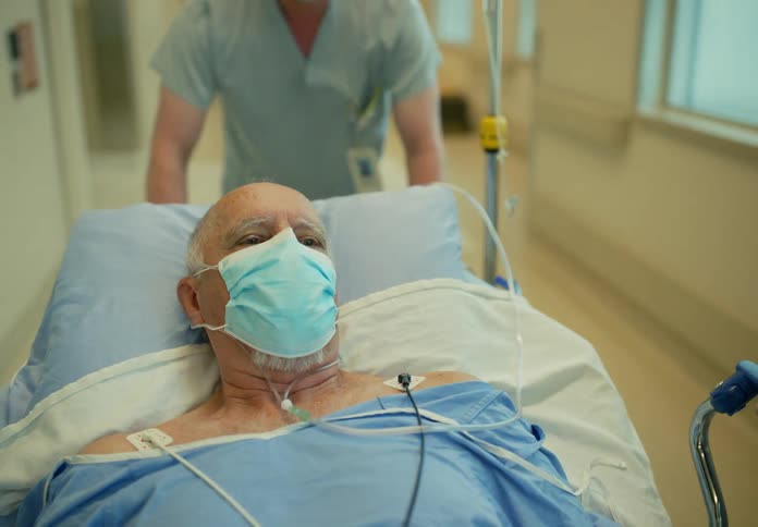 Medical personnel move elderly patient along hospital corridors