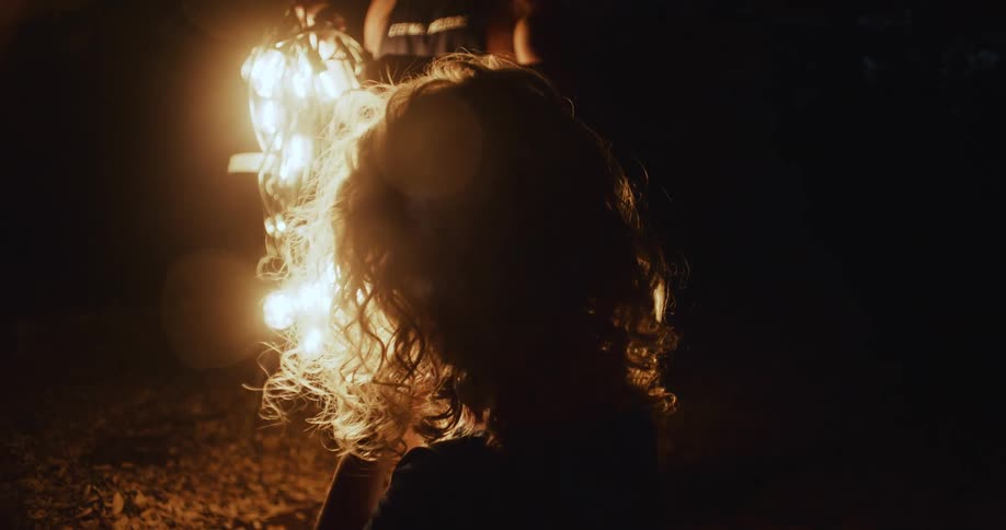 A child outside at night with two other people as they untangle bright lights
