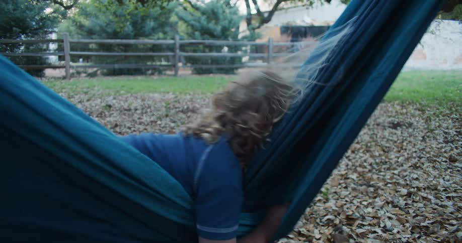Child plays in hammock hanging over fallen leaves in yard as hair stands straight up due to static