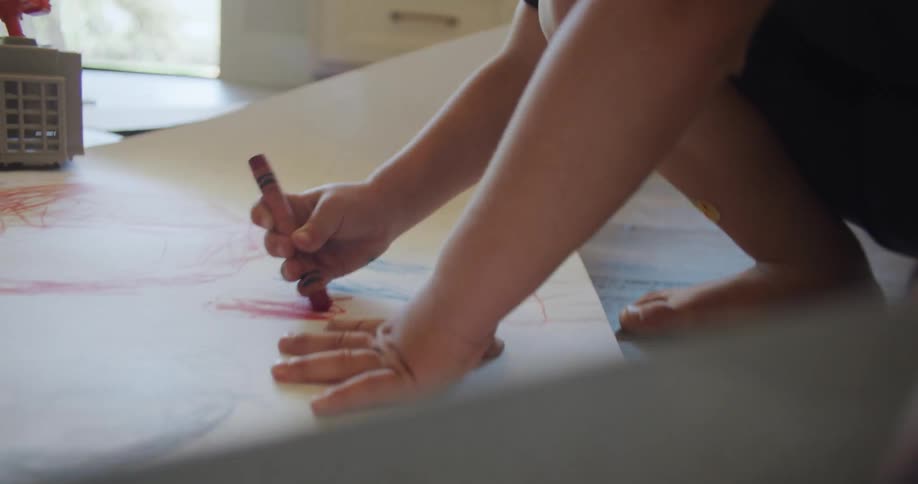 A child is bending down over a large sheet of paper and coloring with a crayon