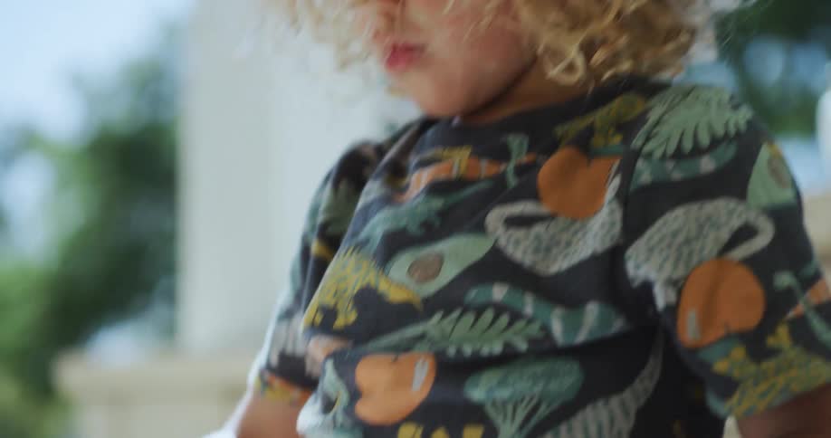 A boy draws on the porch while older children run behind him