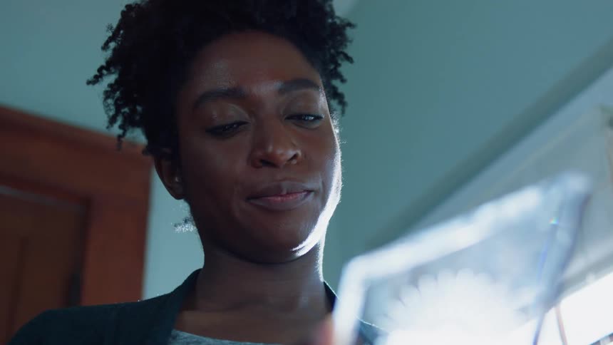 A woman is standing in a room holding a glass picture frame and shaking her head
