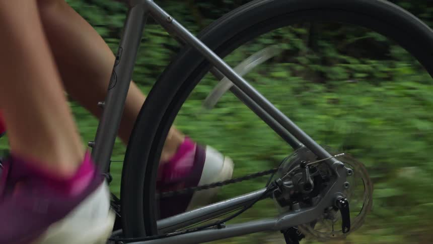 A woman is pedaling a bicycle and there is a pink water bottle on her bike