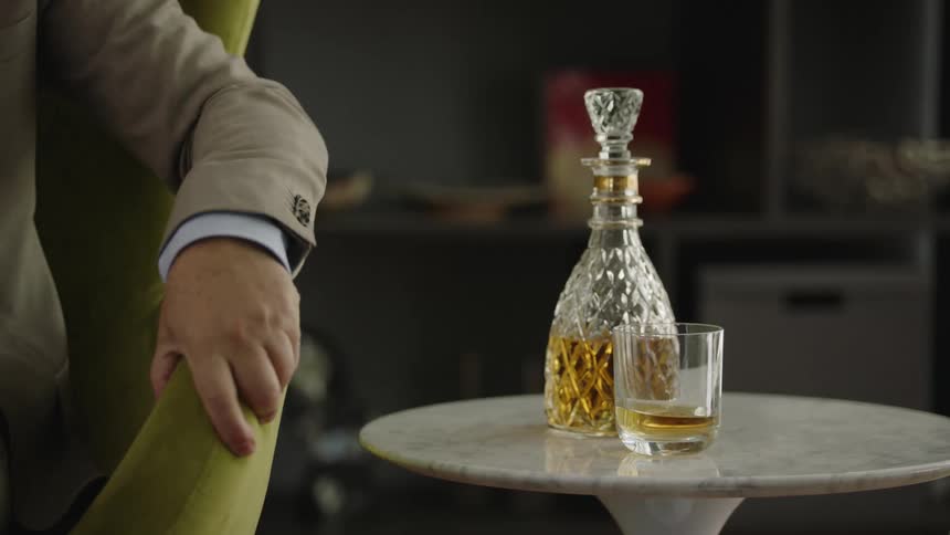 A man at home sets down his alcoholic drinks and gets up from his chair