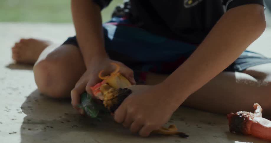 Boy plays with toy figures on ground near wall with water spraying in the background