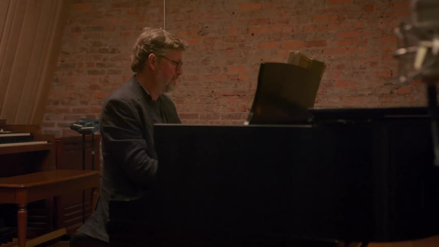 Male pianist sits at grand piano playing with another smaller piano in the background