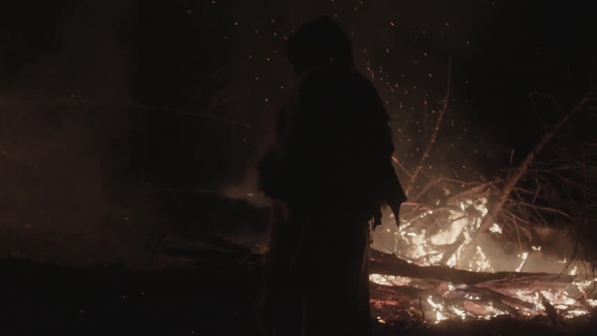 A man standing in front of a pile of burning brush at night