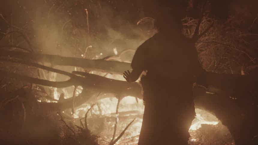 A man warms his hands by a large fire at night