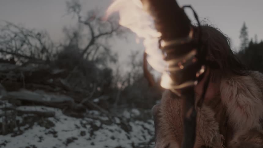 A man holding a burning torch as he surveys a wintry landscape