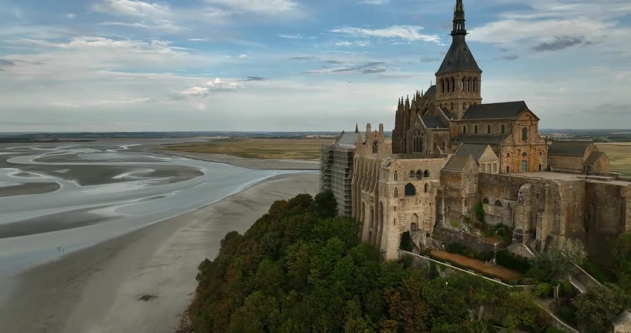Birds fly over cathedral complex overlooking water under a cloudy sky