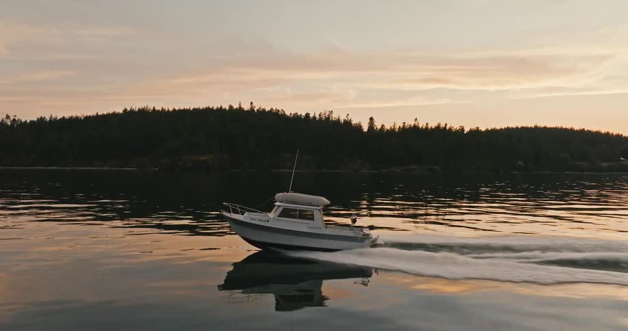 Motorboat travels on water next to forest being silhouetted agains the red sky at sunset