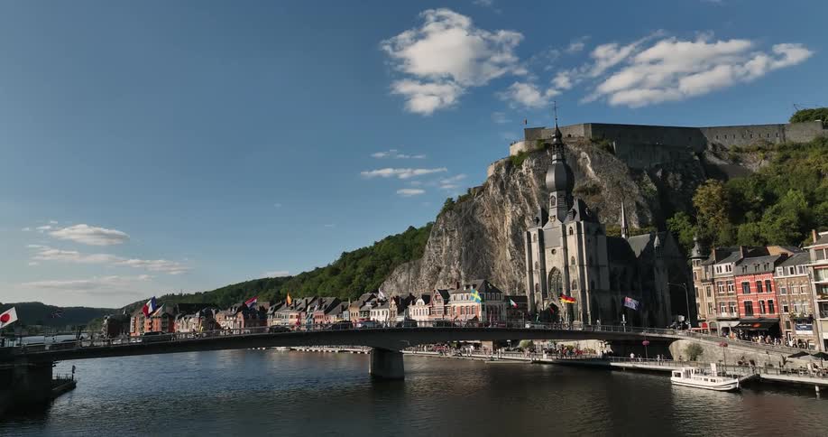 People move along waterfront near religious building and busy bridge