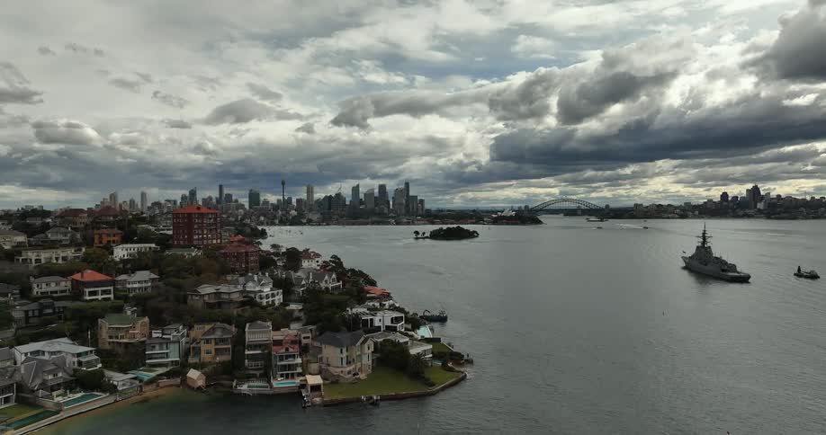 Boats and ships on the ocean next to a neighborhood close to the city skyline at evening