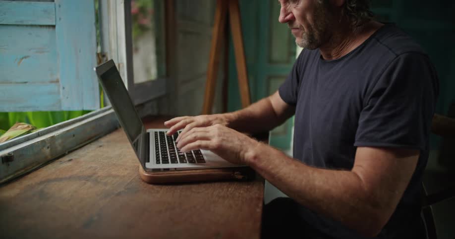 A man is sitting at a table typing on a laptop computer