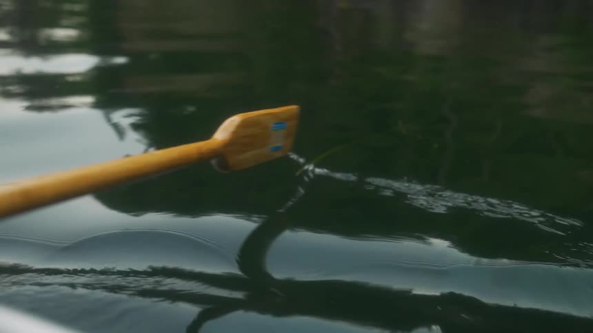 An oar splashes as it moves in the water as someone is rowing a boat