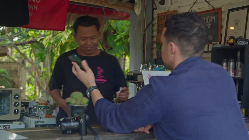 A man sitting at the counter shows the screen of his phone to the bartender
