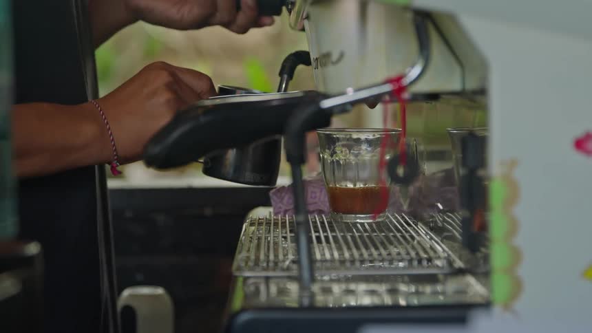 A barista turns on a knob releasing steam then holds a cup under the milk frother