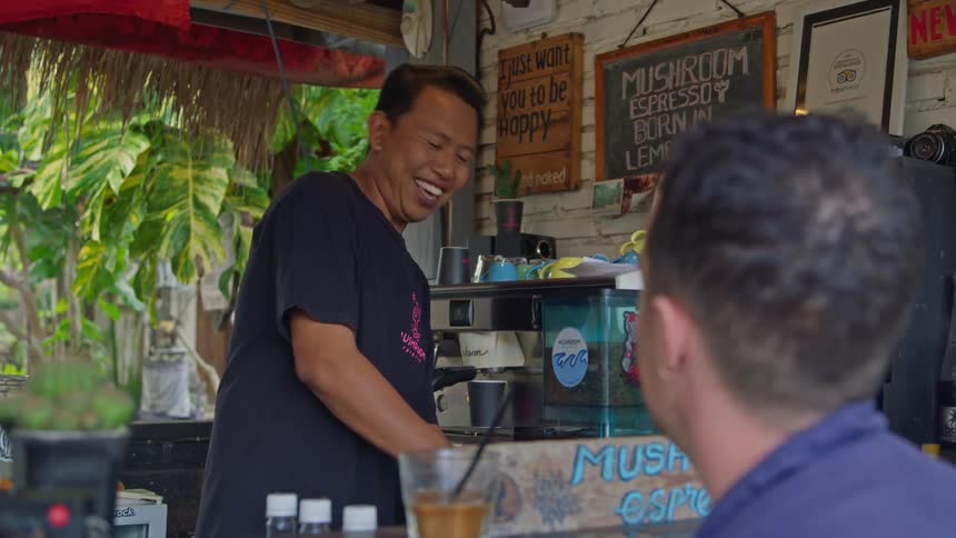 Restaurant owner prepares coffee on an espresso machine for a customer on an outdoors tropical restaurant