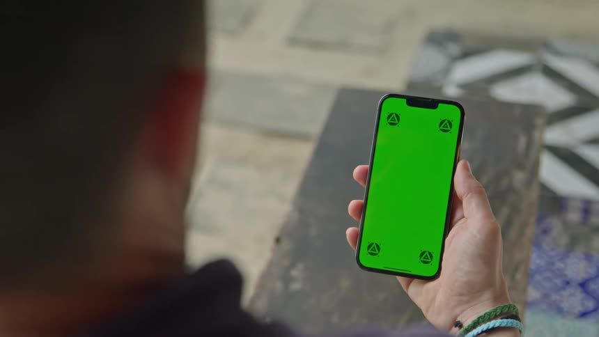 A man is holding a cell phone with a green screen