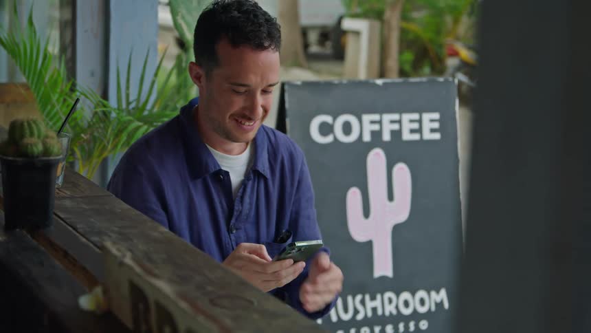 A man waves at someone while scrolling through his phone outside a restaurant