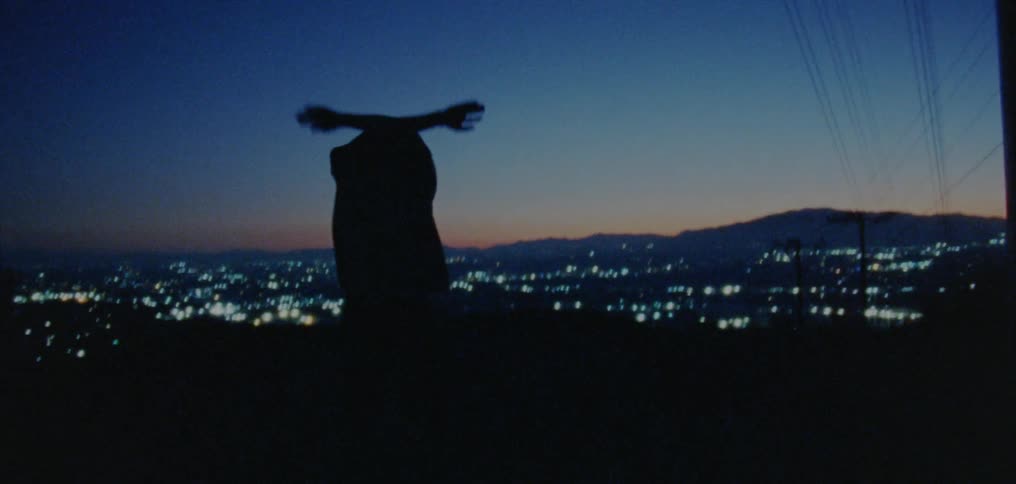 Silhouette of a young man dancing on the countryside near a town at nightfall