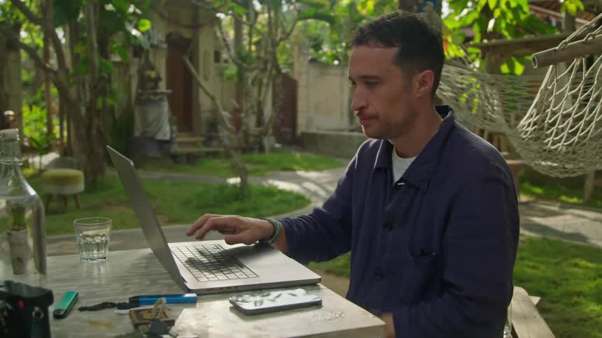 A man is sitting outside at a table typing on a laptop computer