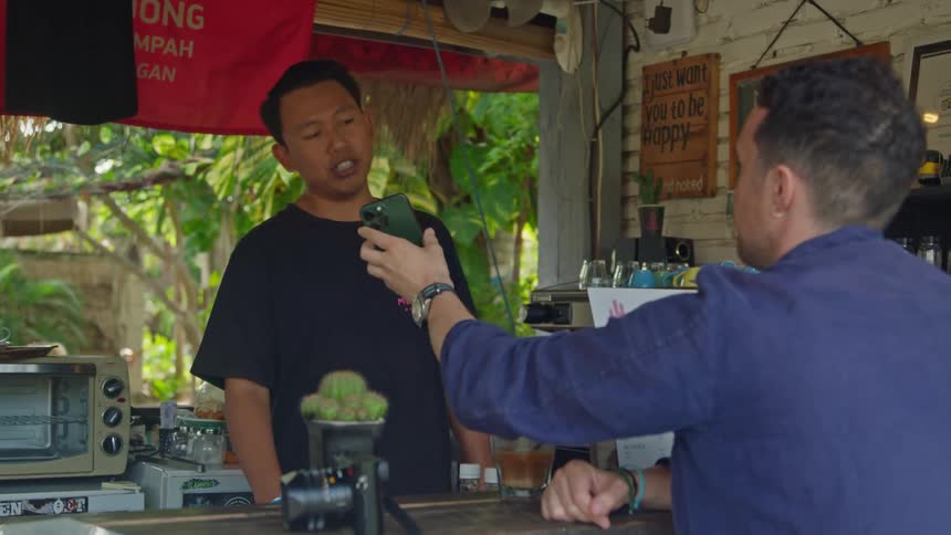 Tourist shows a waiter on a small outdoors cafe a picture on the smartphone