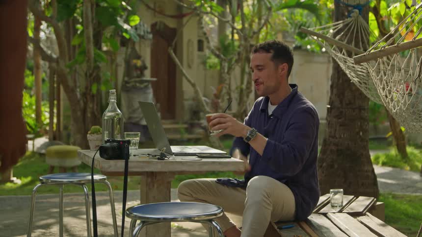 Waiter brings a coffee to a man working on a laptop on an outdoors tropical restaurant