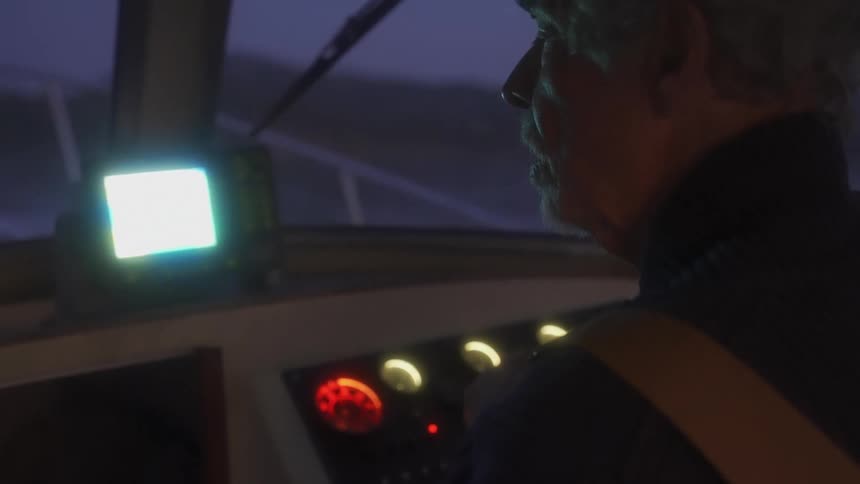 Light of navigation instruments shine on an elderly fisherman driving a boat on a lake at night