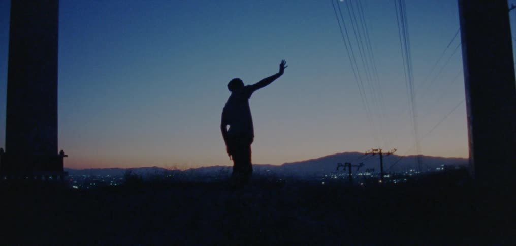 A man dances under power lines in front of a skyline