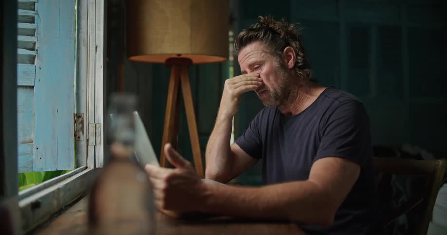 A man rubs the bridge of his nose as he thinks then begins typing