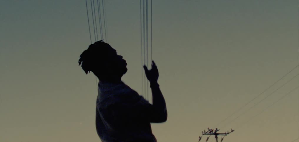 Male dancer partly silhouetted against red tinted sky dances under power lines
