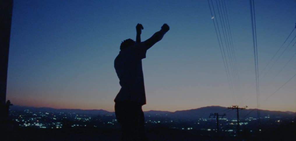 Silhouette of a young man dancing on the countryside near a town at nightfall