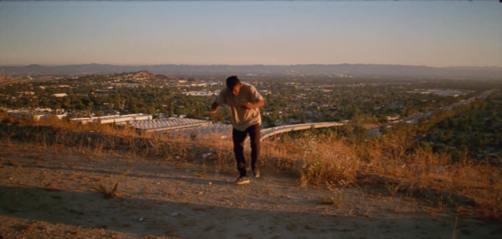 A man dancing on a hill side trail overlooking city highways and buildings