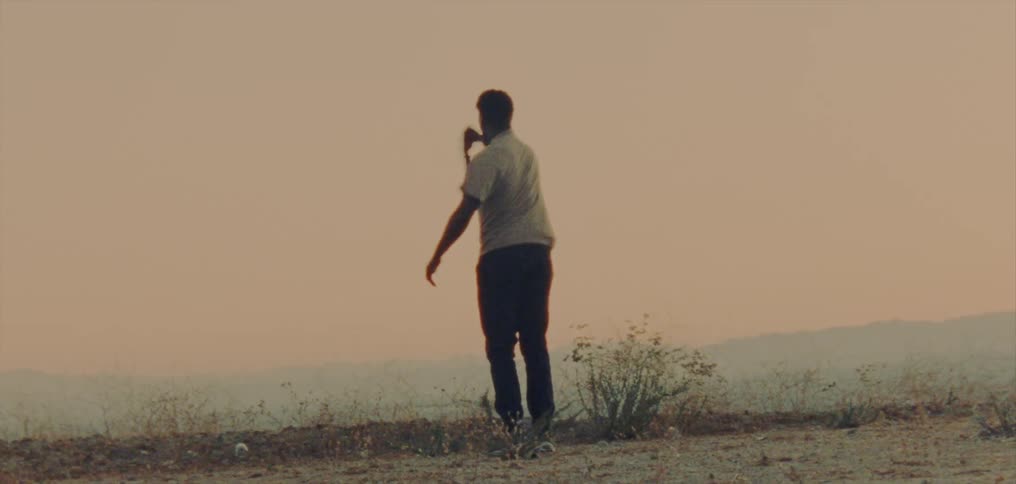 Young man wearing a white shirt dancing on a hill near the foggy mountains at evening