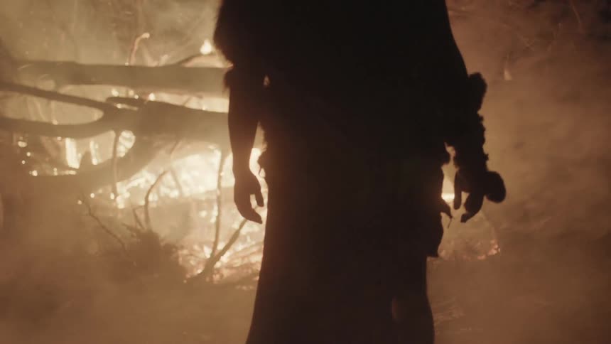 A man walks towards bonfire through the smoke