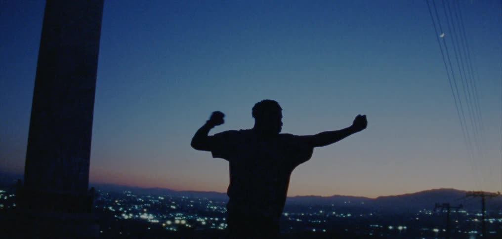 The silhouette of a young man dancing and expressing himself on a hillside above a valley of city lights