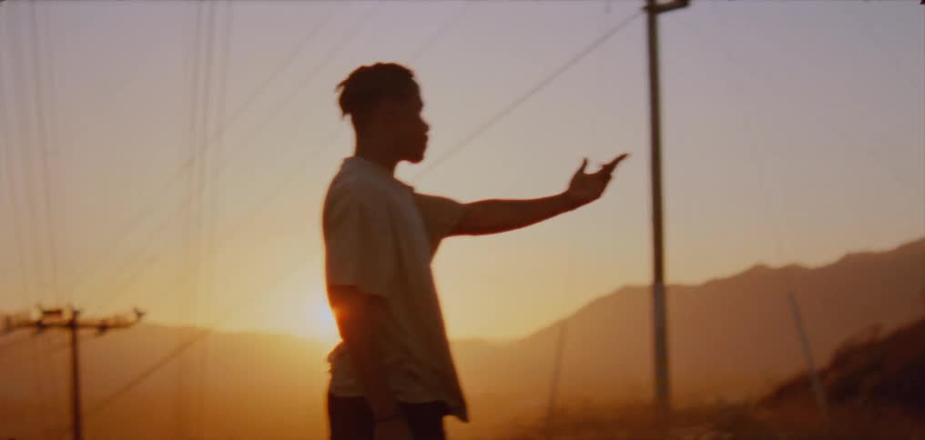 The silhouette of a man standing in profile with sun shining behind him moving his hands and arms to music