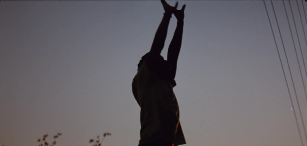 A young man stretches his arms up into the sky moving his hands expressively as he dances