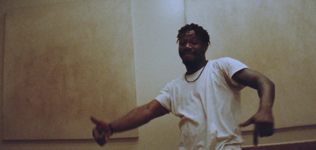 A black man is dancing and making gestures with his arms and hands while smiling