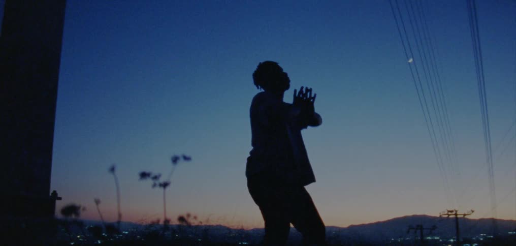 Silhouette of a young man dancing on the countryside near a town at evening