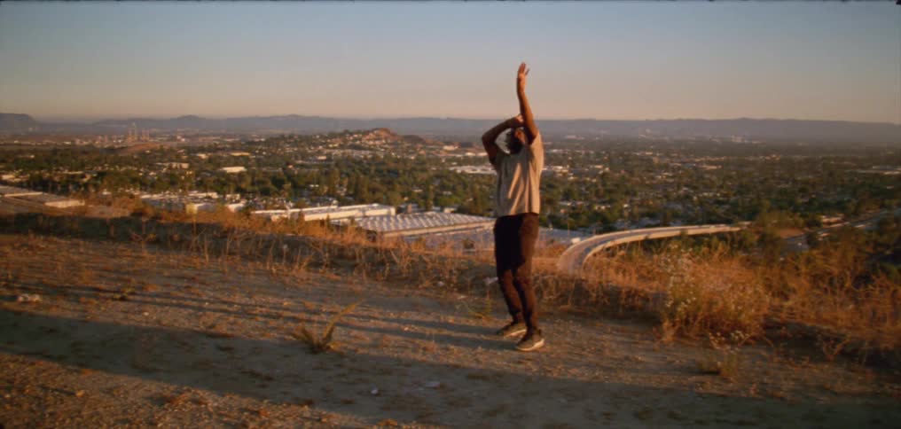 A man is outside in front of a wide shot of land dancing