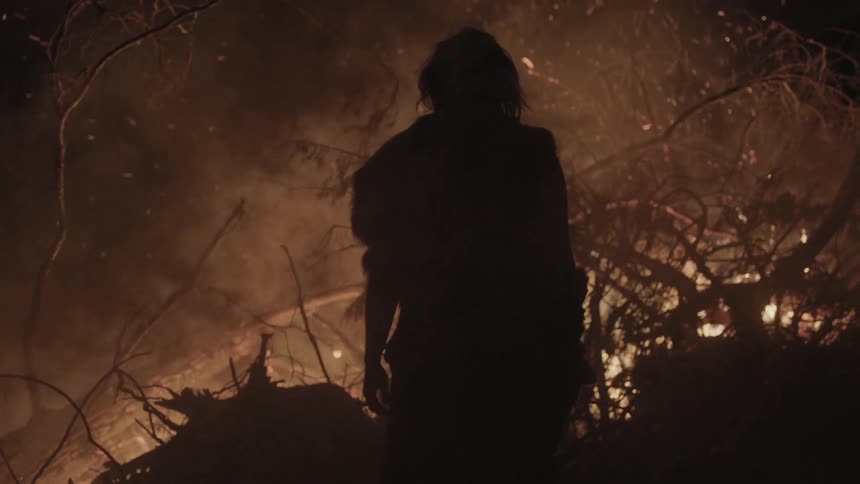 A man stands still in front of a raging bonfire