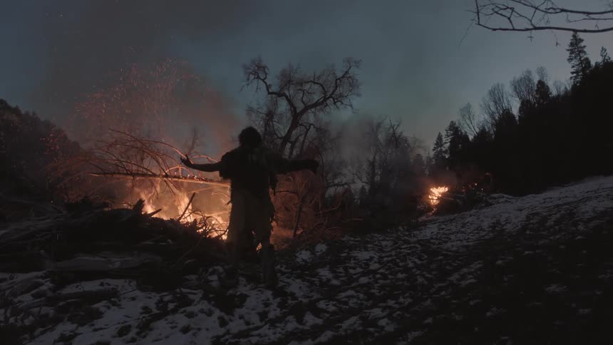 A man lifts his arms near a fire