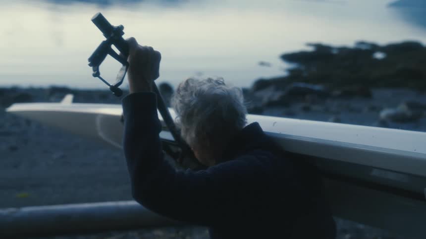 Elderly man carries a kayak to the coast of a lake at morning