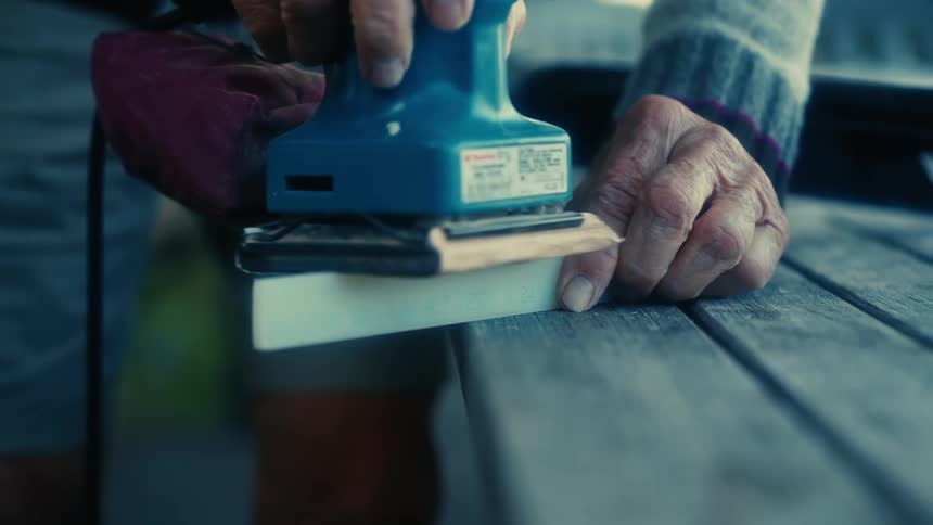 A person is using an electronic sander on the wood