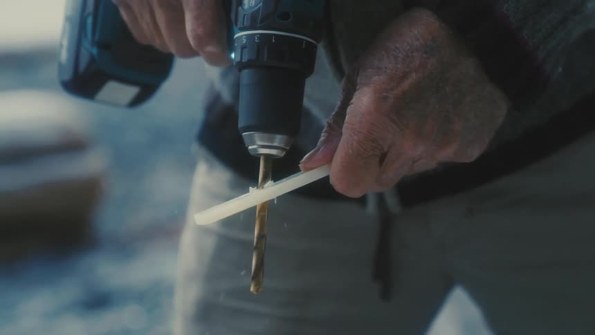 Man wearing gray jacket and brown pants drills through plastic using drill