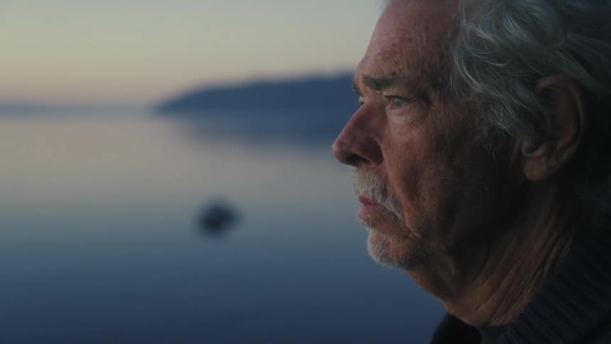 An elderly man stands on the shore and looks out at the ocean