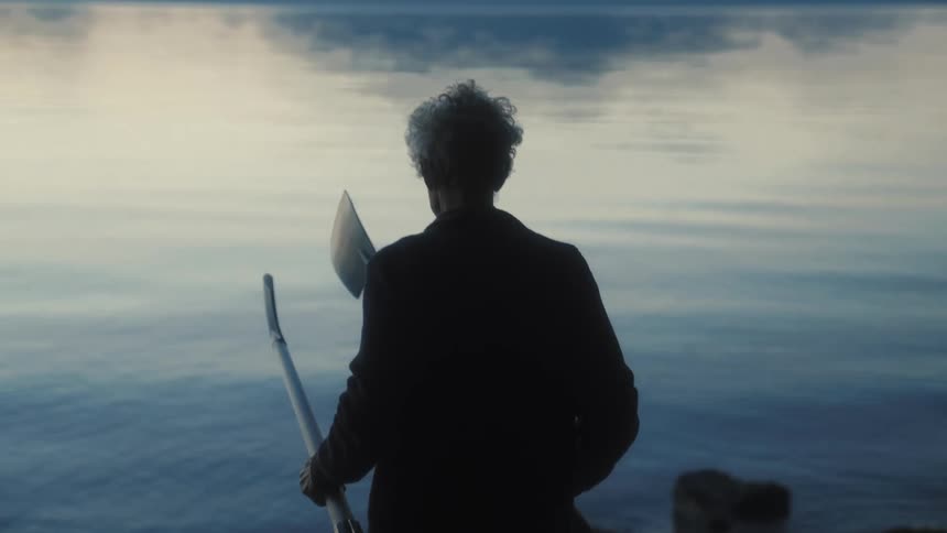 A man walking toward the water carrying two boat oars