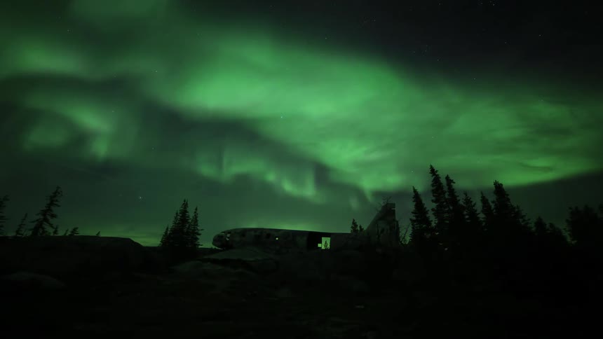 Time lapse of green polar lights aurora borealis shining above an abandoned dismantled airplane on a forest